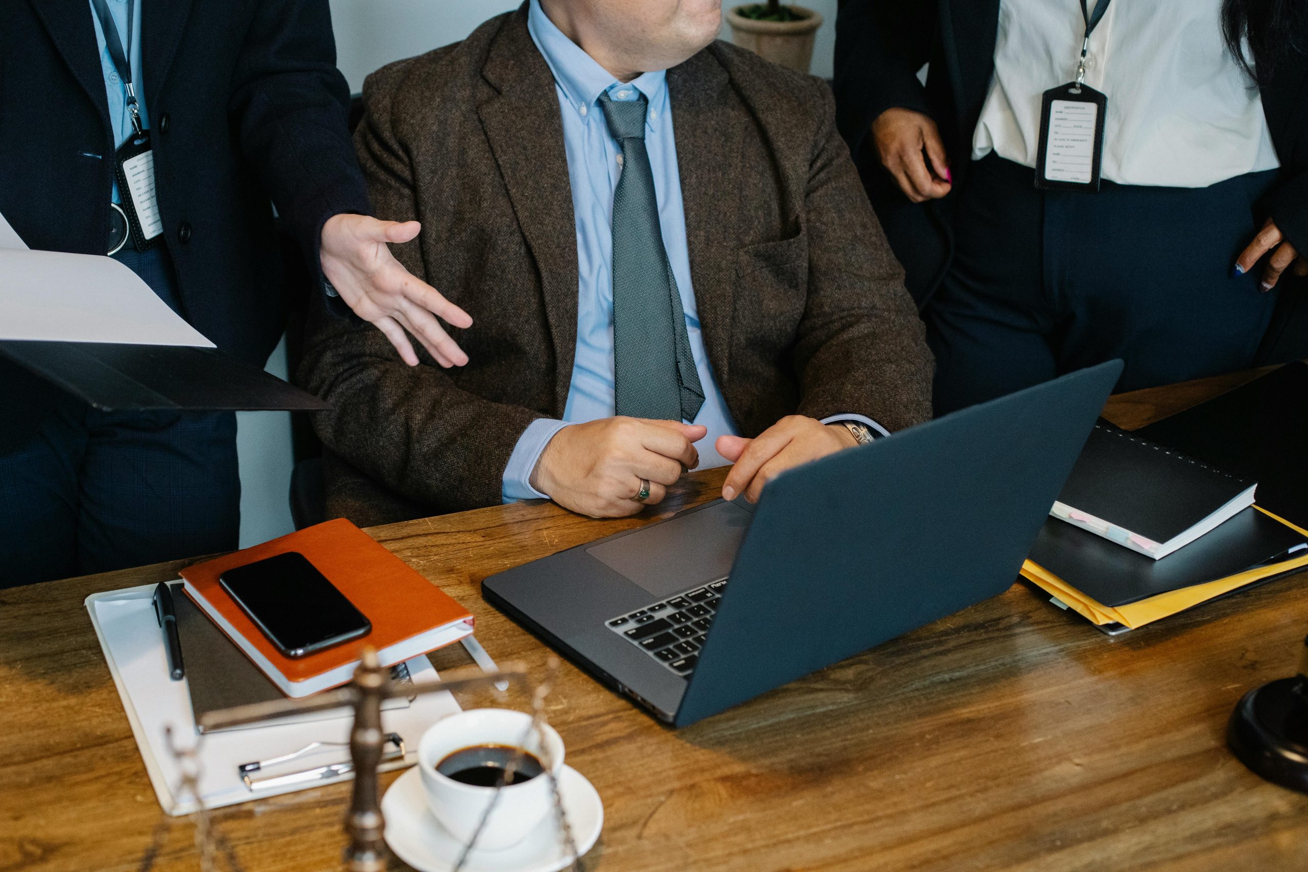 Crop faceless diverse colleagues in formal suits gathering around table with laptop and stack of documents and negotiating about business strategy