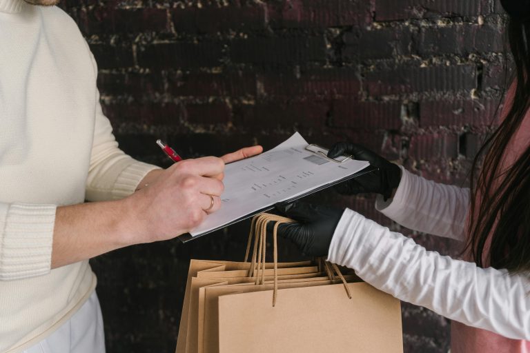 Close-up of a customer signing for delivery, exchanging paper bags indoors.